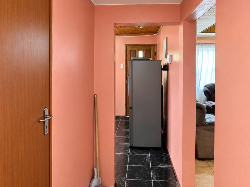 A functional hallway featuring dark tiled flooring and peach-toned walls, providing access to adjacent living areas and rooms.