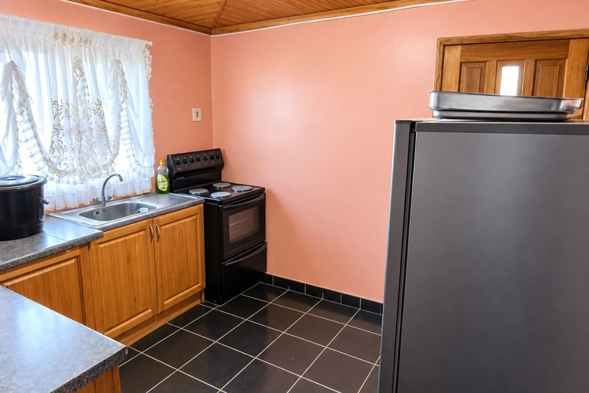 A functional kitchen featuring wooden cabinetry, laminate countertops, a freestanding stove, and a distinctive wooden tongue and groove ceiling with tiled flooring.