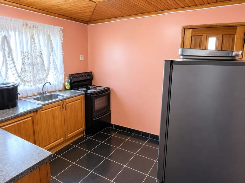 A functional kitchen featuring wooden cabinetry, laminate countertops, a freestanding stove, and a distinctive wooden tongue and groove ceiling with tiled flooring.