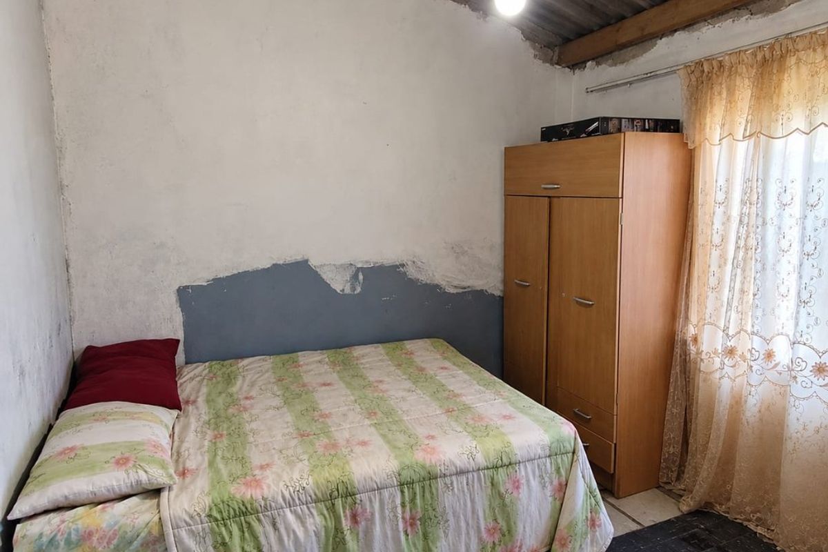 A bedroom featuring exposed roof structure, unfinished wall plaster, and tiled flooring, requiring renovation to improve the overall finish and condition.