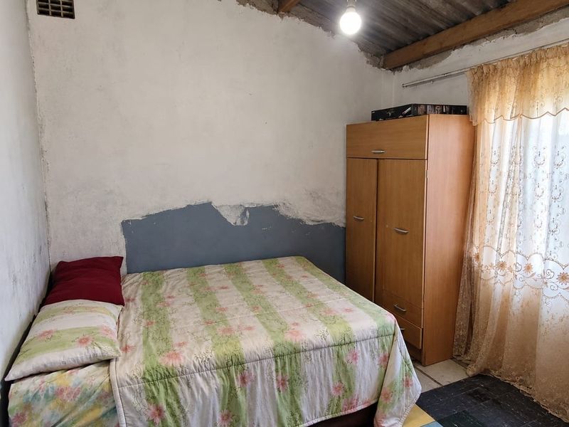 A bedroom featuring exposed roof structure, unfinished wall plaster, and tiled flooring, requiring renovation to improve the overall finish and condition.