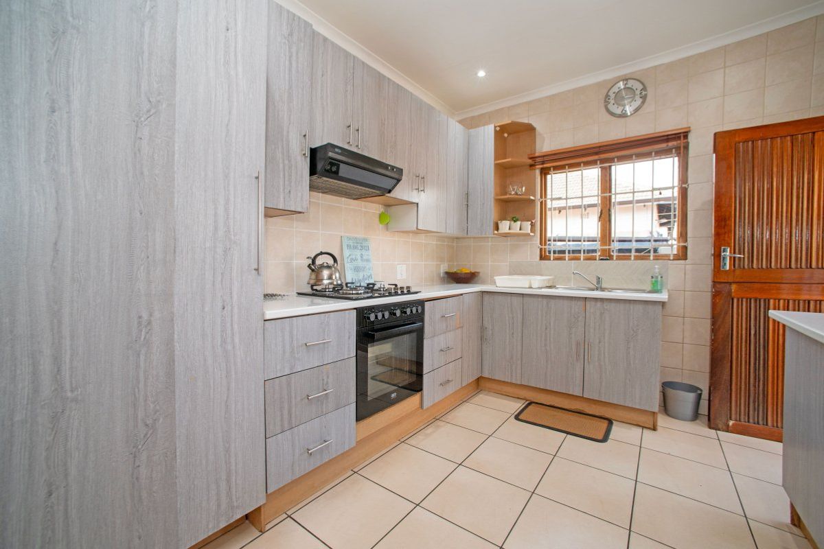 Functional kitchen featuring light wood-grain cabinetry, built-in oven with gas hob, tiled backsplash, and tiled flooring with a window security gate.