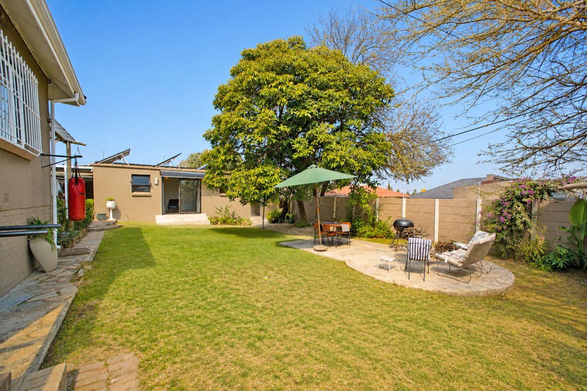 A spacious rear garden featuring a well-maintained lawn, a paved patio area, mature trees, and perimeter precast concrete walling.