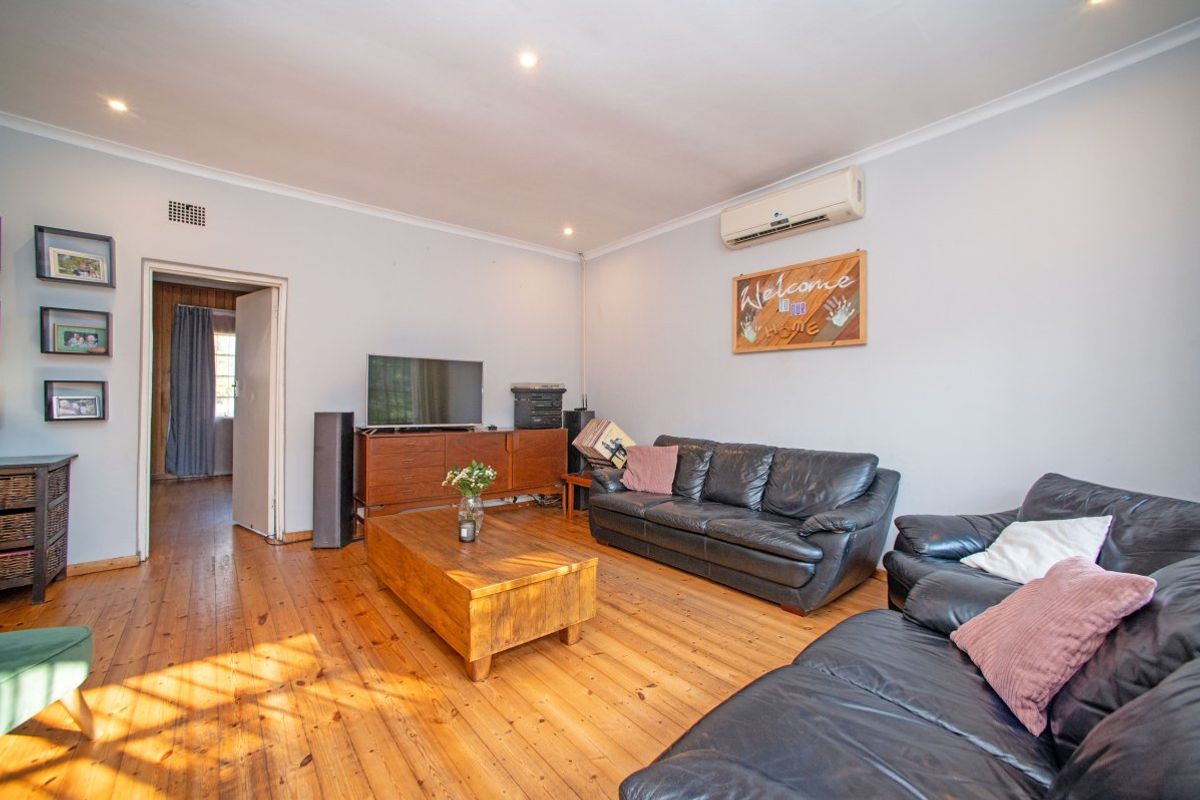 A spacious living room featuring polished hardwood flooring, recessed downlighting, and a wall-mounted split-system air conditioning unit.