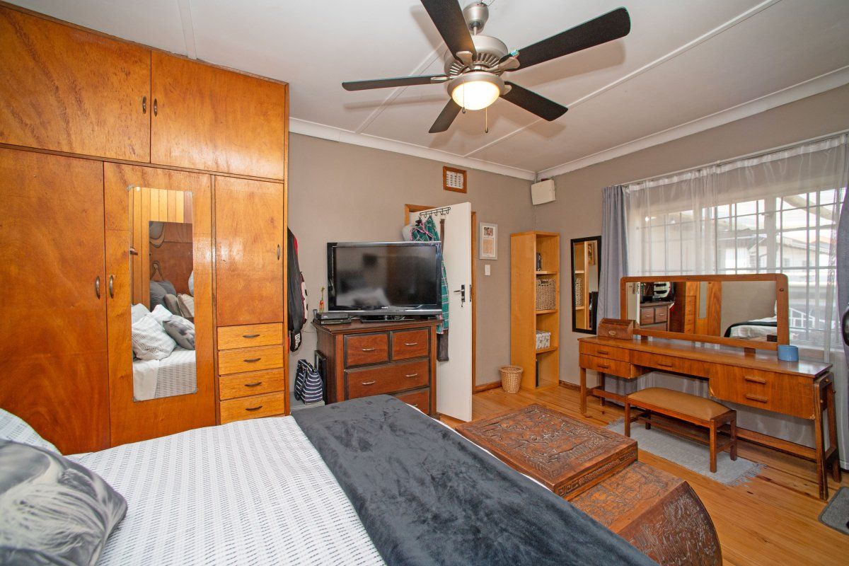 A bedroom featuring built-in wooden cupboards, a ceiling fan, and wooden flooring, offering a functional and traditional living space.