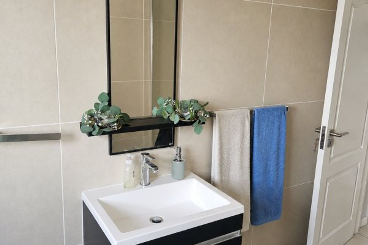 A modern bathroom featuring a wall-mounted vanity with a ceramic basin, chrome mixer tap, and large wall-mounted mirror against neutral tiled walls.