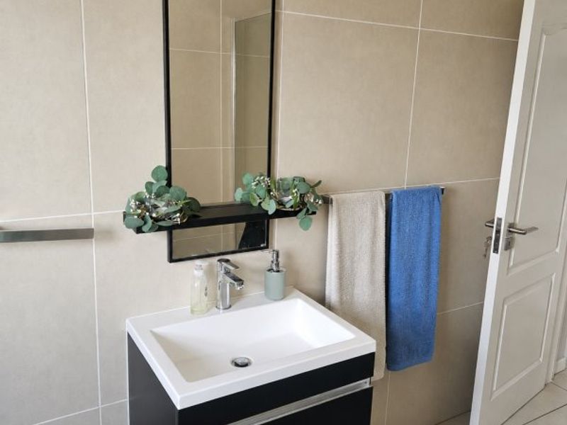 A modern bathroom featuring a wall-mounted vanity with a ceramic basin, chrome mixer tap, and large wall-mounted mirror against neutral tiled walls.