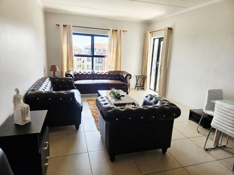 Spacious living room featuring neutral tiled flooring, large windows with natural light, and access to an outdoor area through a sliding glass door.
