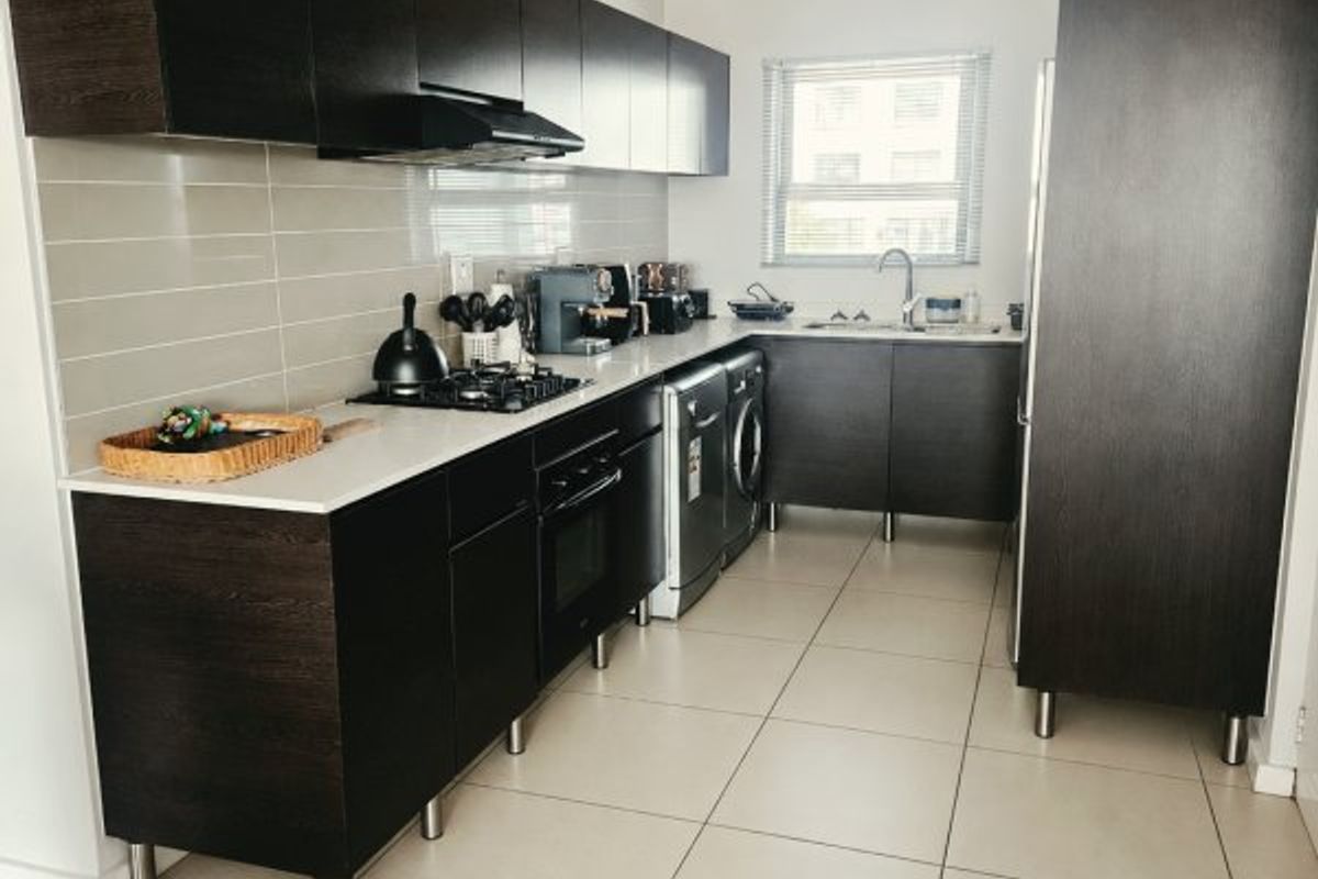 Modern kitchen featuring dark wood cabinetry, integrated appliances, gas hob, built-in oven, and neutral tiled flooring with a clean, functional layout.