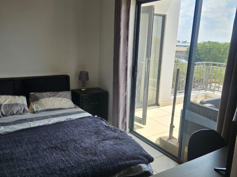 A well-lit bedroom featuring tiled flooring and a large sliding glass door that provides direct access to a private balcony.