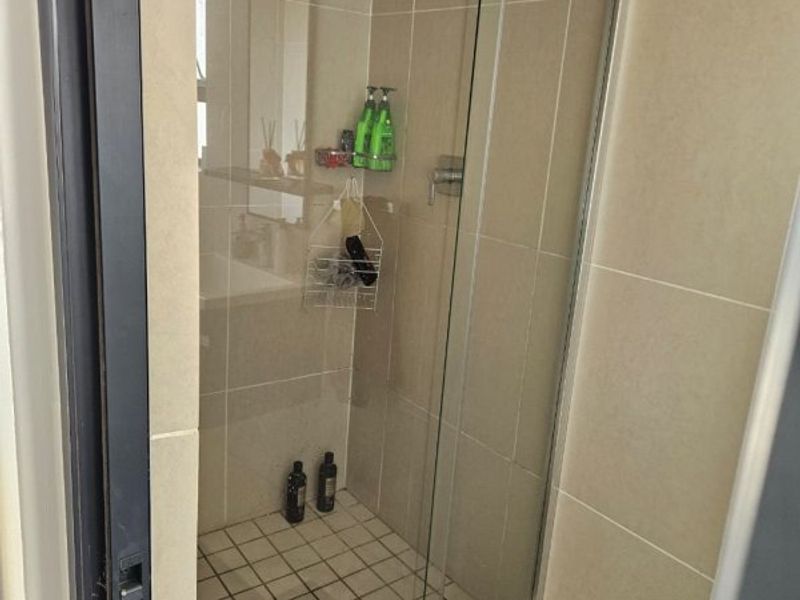 A functional bathroom shower enclosure featuring neutral wall tiling and a standard shower head fixture.