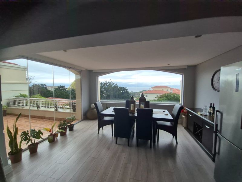 A bright dining area featuring light laminate flooring, recessed lighting, and large windows offering scenic views, with seamless access to an outdoor balcony.
