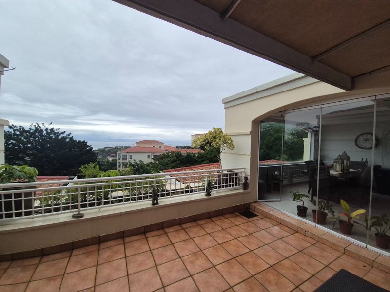 A spacious covered balcony featuring tiled flooring, a protective metal balustrade, and glass sliding doors, offering elevated views of the surrounding neighborhood.