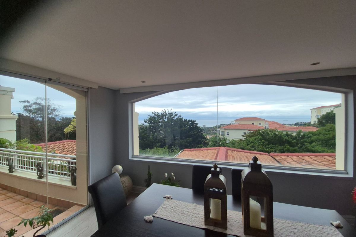 A bright living area featuring large windows and sliding glass doors that open onto a balcony, offering expansive views of the surrounding neighborhood.