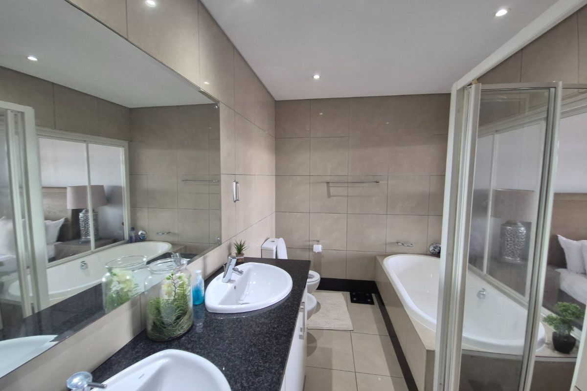Modern bathroom featuring a double vanity with granite countertop, large wall mirror, built-in bathtub, and a separate shower enclosure with tiled finishes.