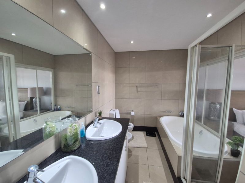 Modern bathroom featuring a double vanity with granite countertop, large wall mirror, built-in bathtub, and a separate shower enclosure with tiled finishes.