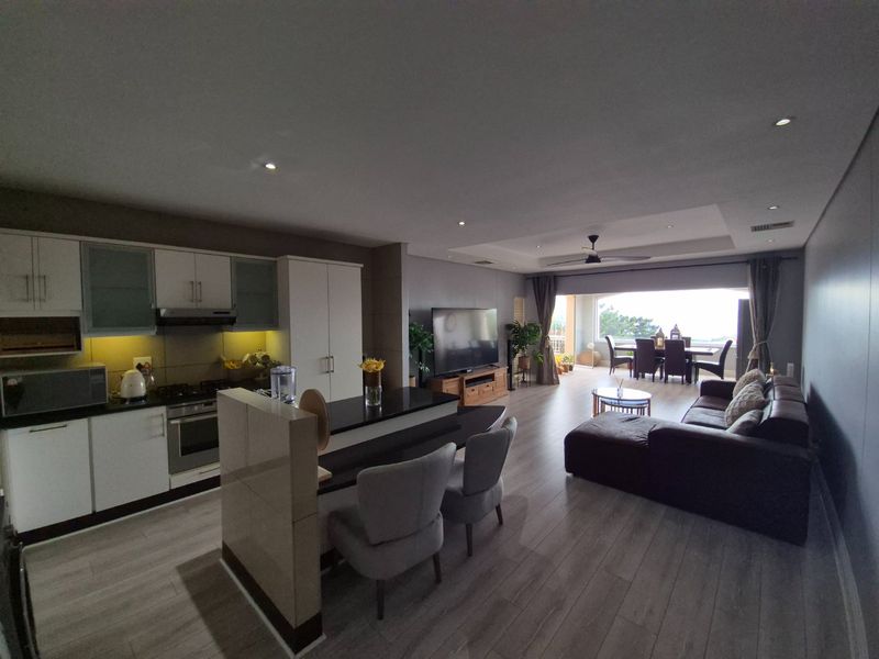 Spacious open-plan living area featuring a modern kitchen with stone countertops, integrated appliances, and seamless flow to the dining space and balcony.