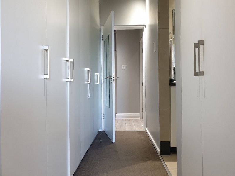 A clean hallway featuring extensive built-in cupboard storage with modern metal handles, leading towards an adjacent room.