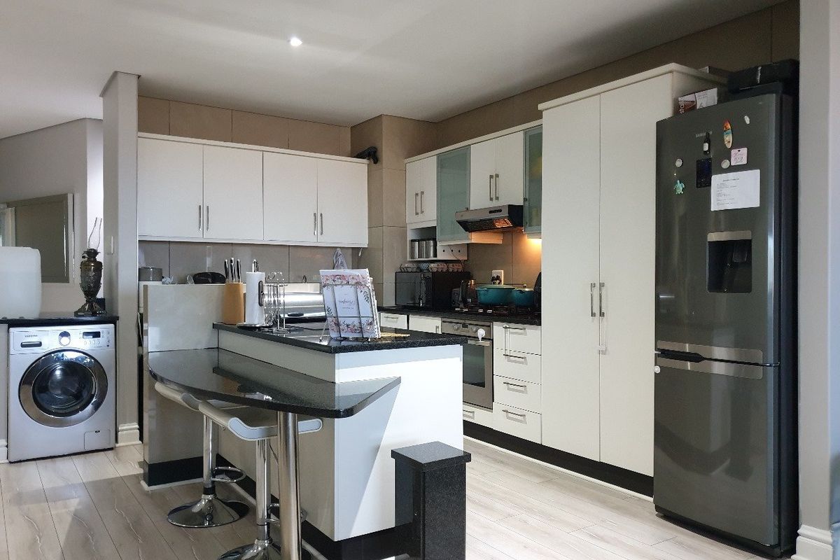 Modern kitchen featuring white cabinetry, granite countertops, a breakfast bar, built-in oven, extractor fan, and integrated laundry facilities.