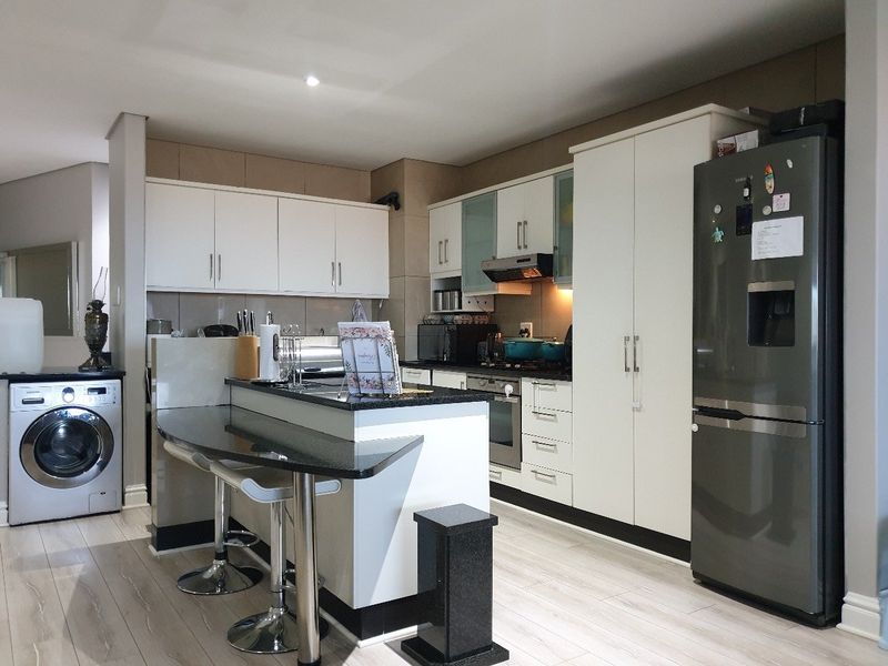 Modern kitchen featuring white cabinetry, granite countertops, a breakfast bar, built-in oven, extractor fan, and integrated laundry facilities.