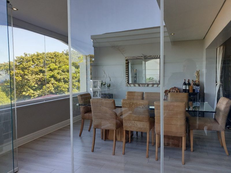A bright, enclosed balcony featuring modern laminate flooring, recessed ceiling lights, and large glass panels offering an expansive view of the surrounding greenery.