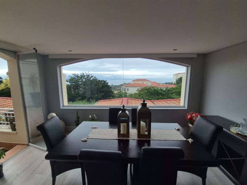 A bright dining area featuring a large picture window with scenic views, recessed lighting, and modern laminate flooring, seamlessly connected to an outdoor balcony.