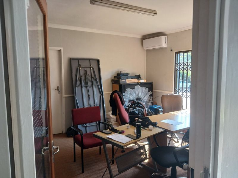 A functional office space featuring carpeted flooring, a wall-mounted air conditioning unit, and security bars on the window.