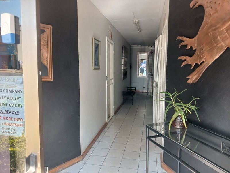 A commercial hallway featuring tiled flooring, security gates, and contrasting black and white wall finishes, providing access to internal office spaces.