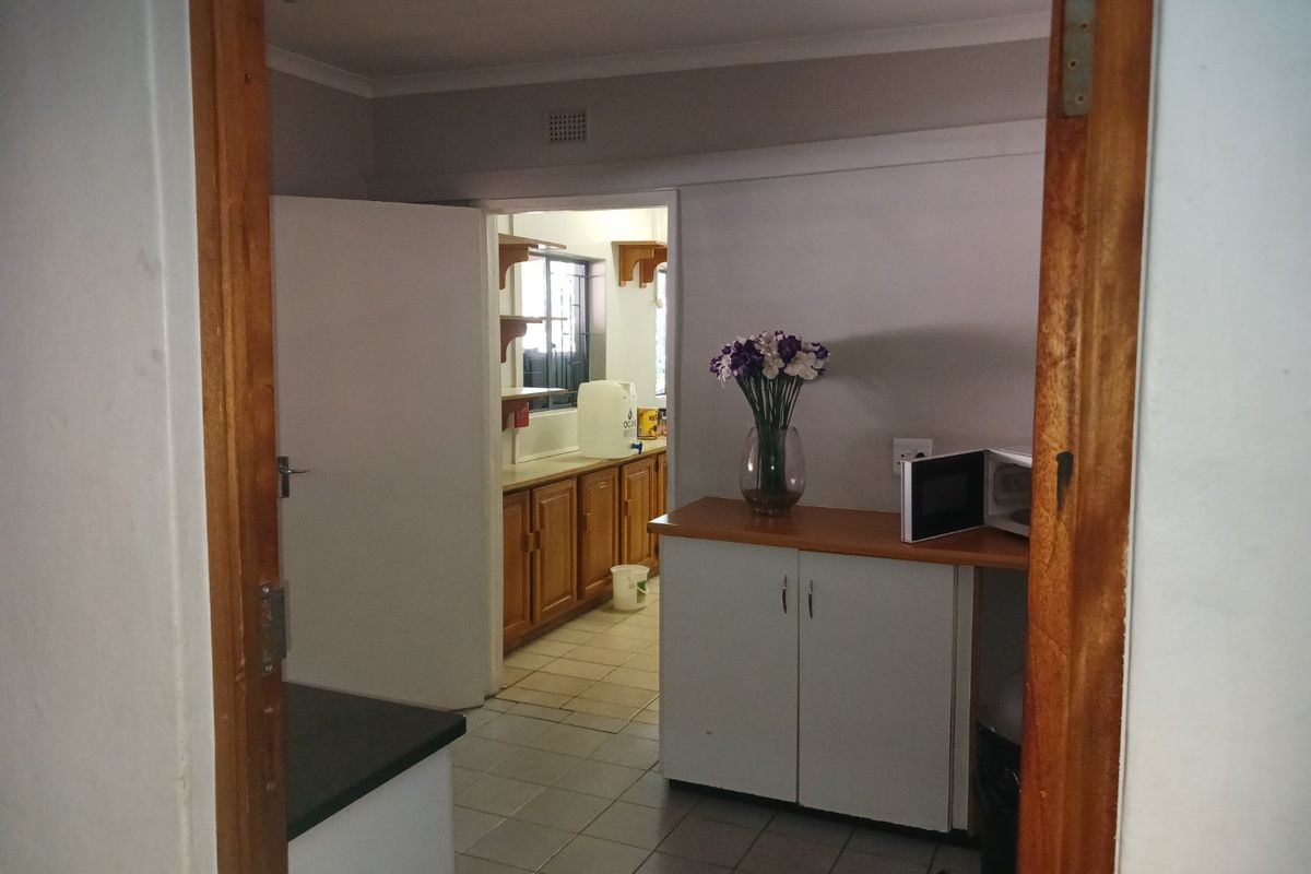 A functional kitchen area featuring built-in cabinetry, tiled flooring, and laminate countertops, viewed through a wooden door frame.