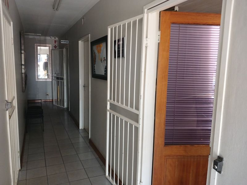 A commercial hallway featuring tiled flooring, security gates, and access to multiple office spaces.