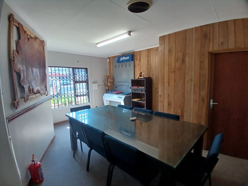 A functional office space featuring wood paneling, carpet flooring, and a security gate on the window, suitable for a professional meeting or workspace.
