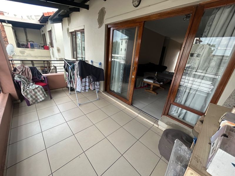 A covered balcony featuring tiled flooring, timber-framed sliding doors, and metal railings, offering an outdoor extension to the living area.
