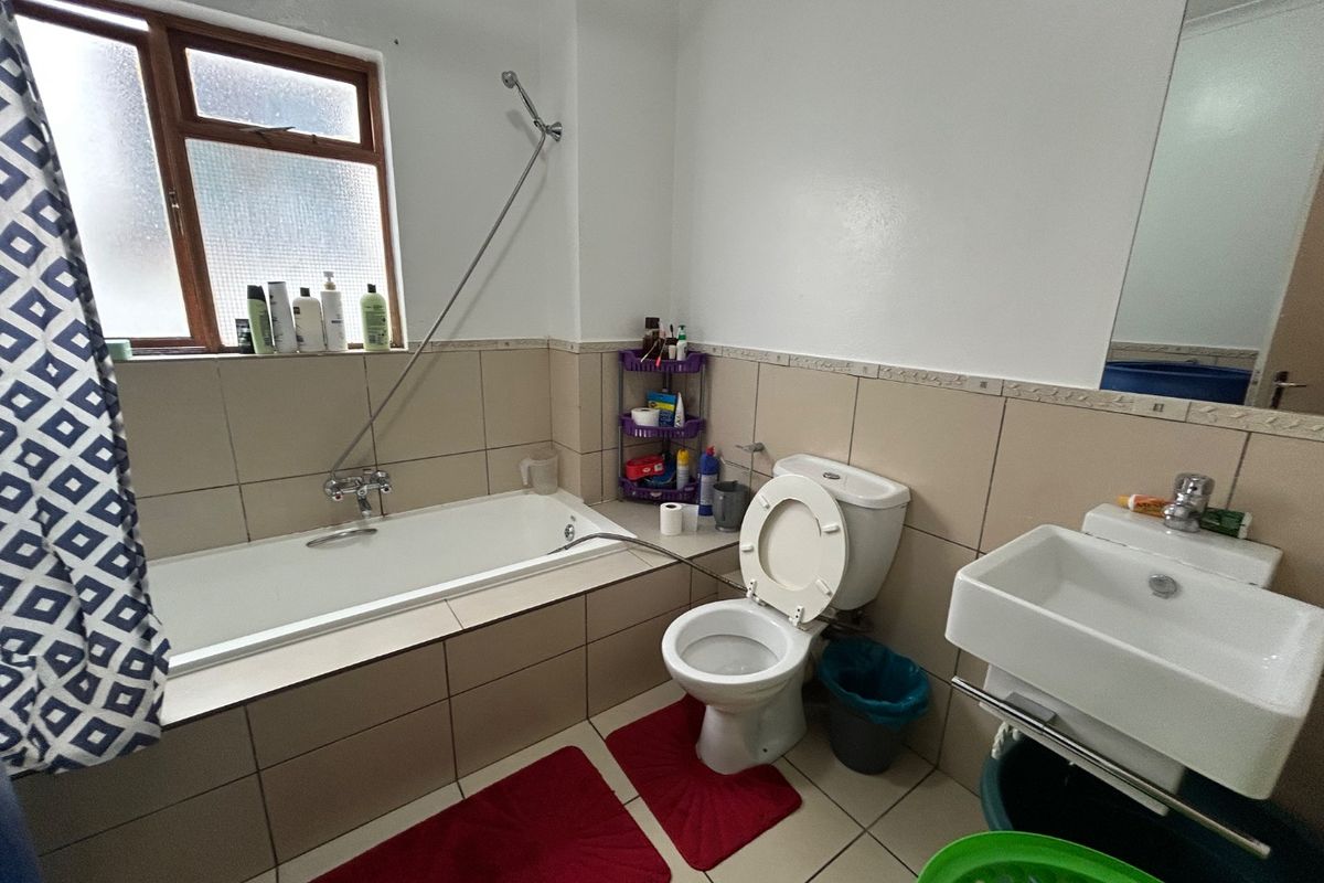 A functional bathroom featuring a built-in bathtub with shower mixer, a wall-mounted basin, and neutral ceramic tiling throughout.