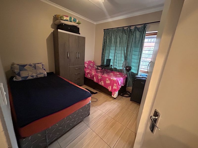 A functional bedroom featuring tiled flooring, a built-in wardrobe, and a window fitted with security bars.