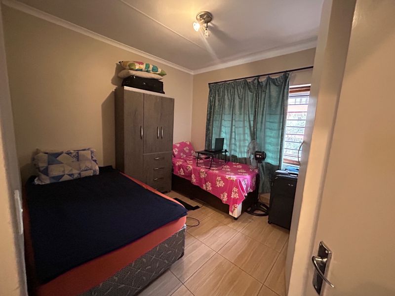 A functional bedroom featuring tiled flooring, a built-in wardrobe, and a window with curtain fittings, providing a practical living space.