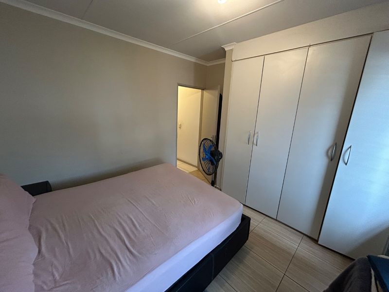 A bedroom featuring built-in cupboards, tiled flooring, and coved ceiling details, offering a functional and neutral living space.
