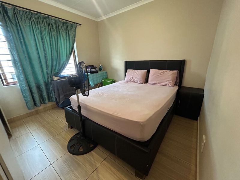 A functional bedroom featuring tiled flooring, cove cornicing, and security burglar bars on the window.