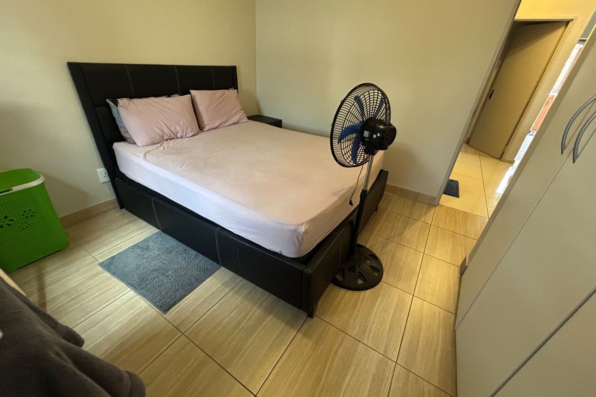 A functional bedroom featuring tiled flooring and a built-in wardrobe, providing a clean and neutral space for rest.