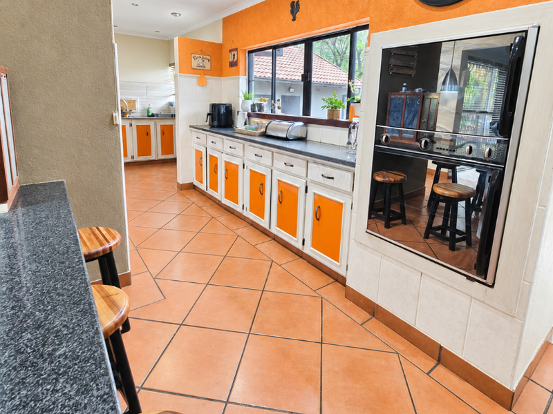 A spacious kitchen featuring vibrant orange cabinetry, granite countertops, tiled flooring, and a built-in oven, offering a functional layout with ample storage space.
