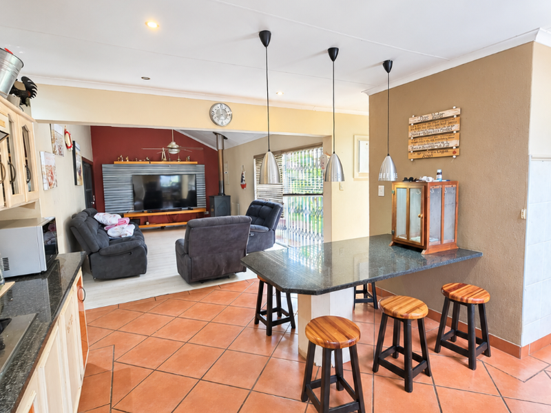 Open-plan living and kitchen area featuring terracotta floor tiles, granite countertops, pendant lighting, and a cozy fireplace, creating a functional family space.