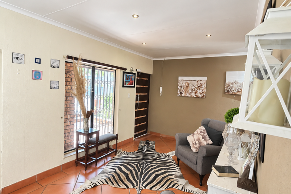 A living room featuring terracotta floor tiles, recessed downlighting, and a sliding glass door with an integrated security gate.