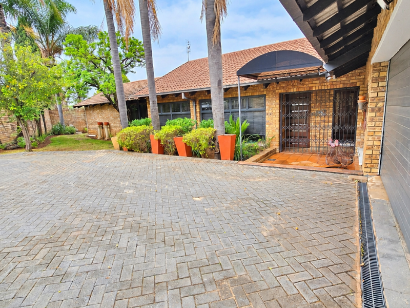 A well-maintained front exterior featuring a spacious brick-paved driveway, facebrick facade, and secure entrance with a tiled roof.