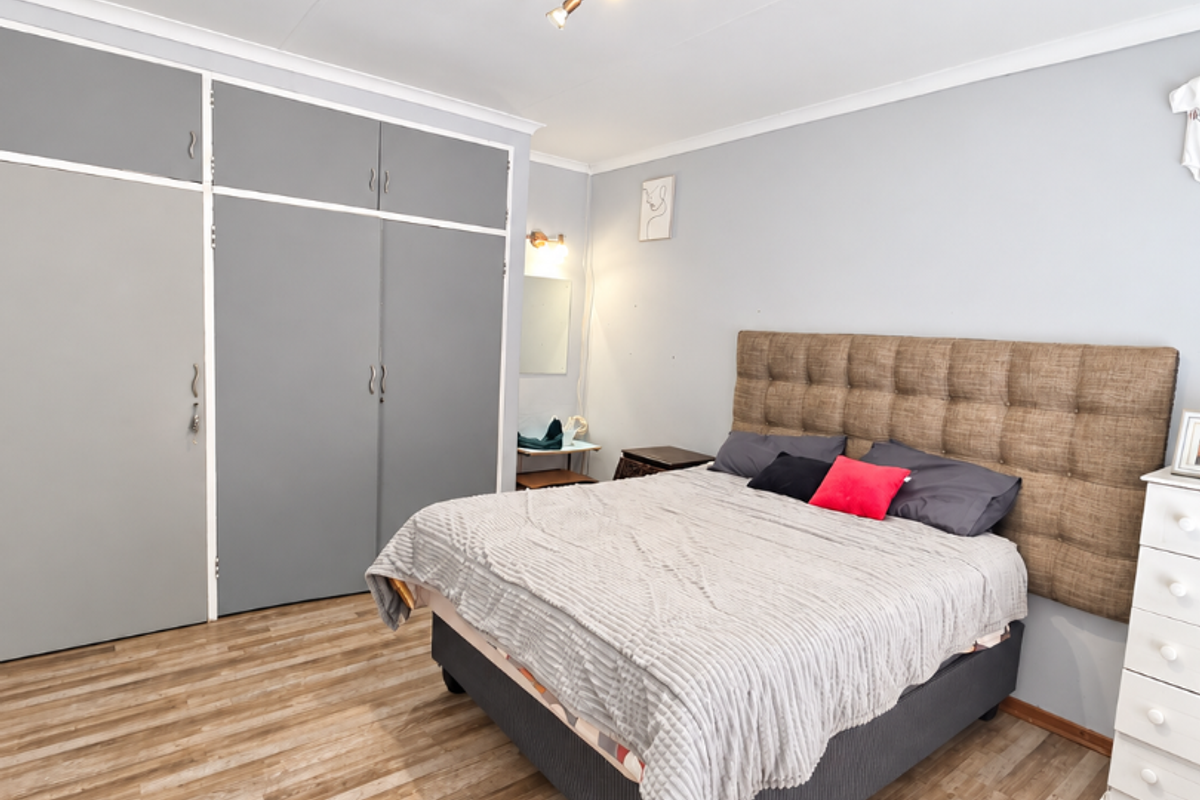 A well-maintained bedroom featuring light-toned laminate flooring, neutral walls, and extensive built-in cupboard storage.