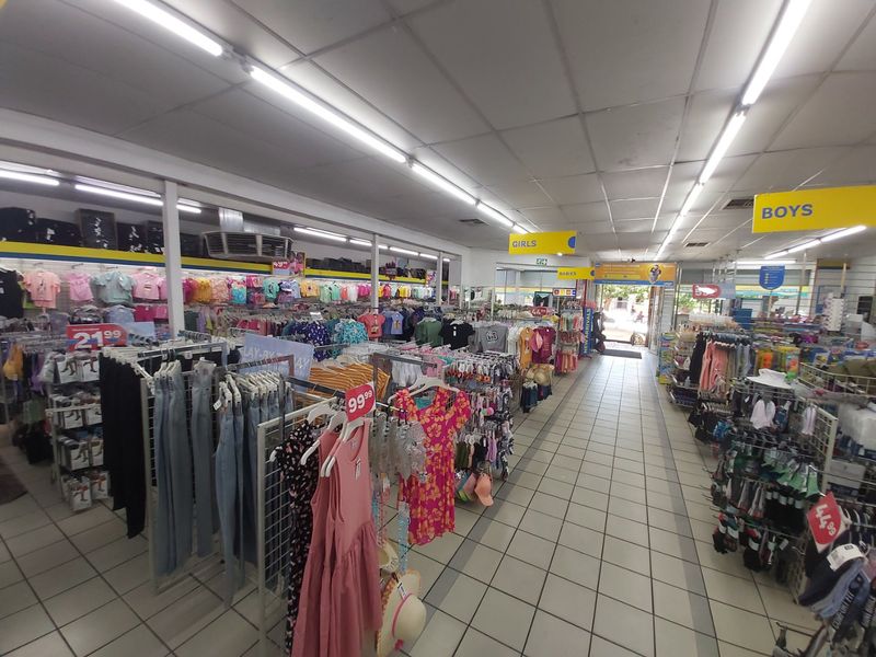 A commercial retail space featuring tiled flooring, suspended ceiling grid, and fluorescent strip lighting, currently utilized as a clothing store.