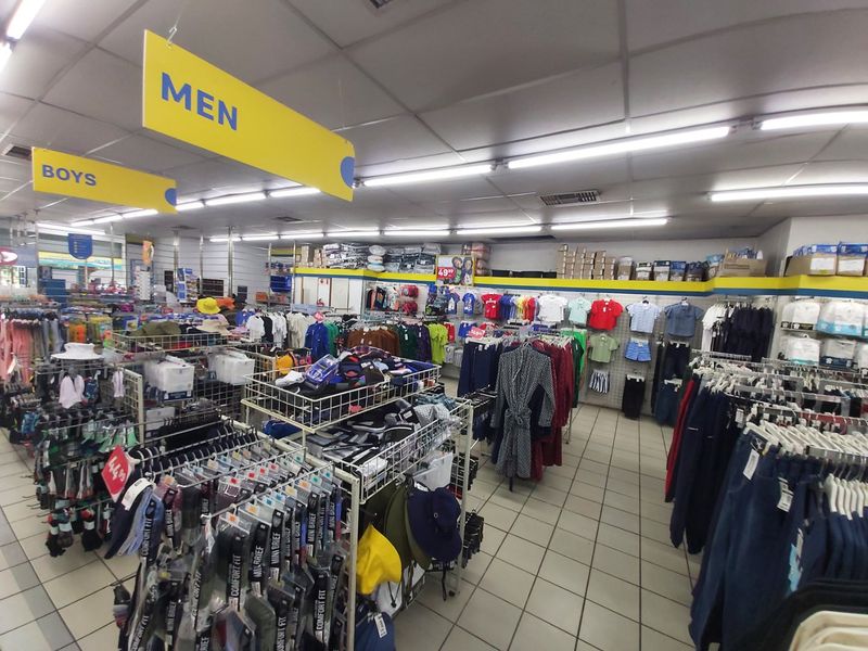 A commercial retail clothing store interior featuring tiled flooring, suspended ceiling with fluorescent lighting, and organized clothing display racks.