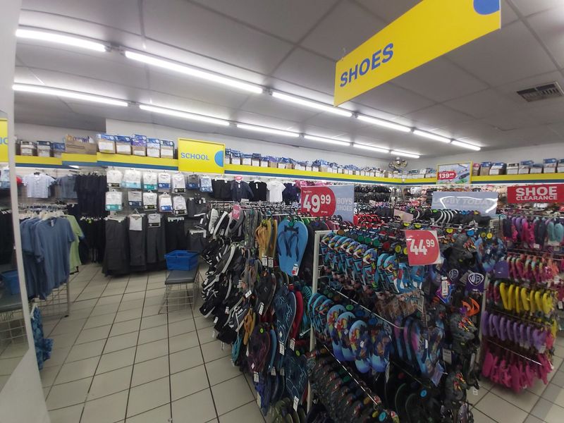 Interior view of a commercial retail space featuring suspended ceilings, fluorescent lighting, and tiled flooring, currently utilized as a footwear and clothing store.