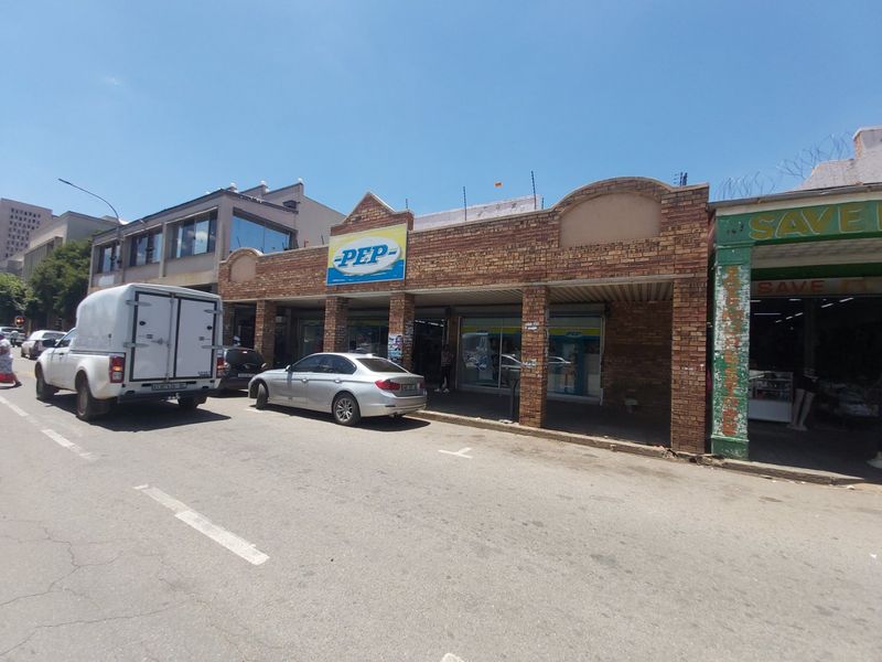 Street-level view of a commercial retail storefront featuring a brick facade and covered walkway in a busy urban setting.