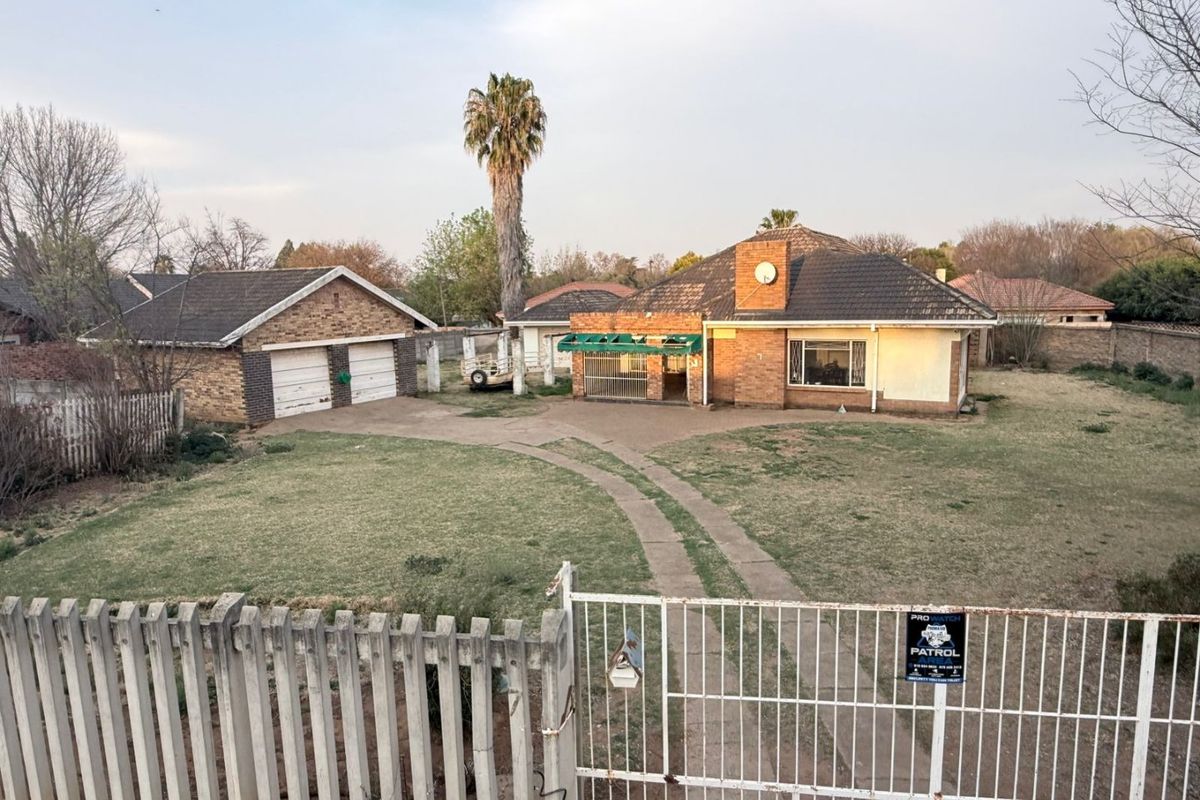 Front view of a single-story brick house featuring a double garage, concrete driveway, and gated entrance on a spacious residential lot.