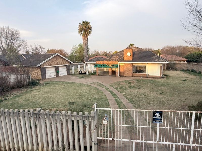 Front view of a single-story brick house featuring a double garage, concrete driveway, and gated entrance on a spacious residential lot.
