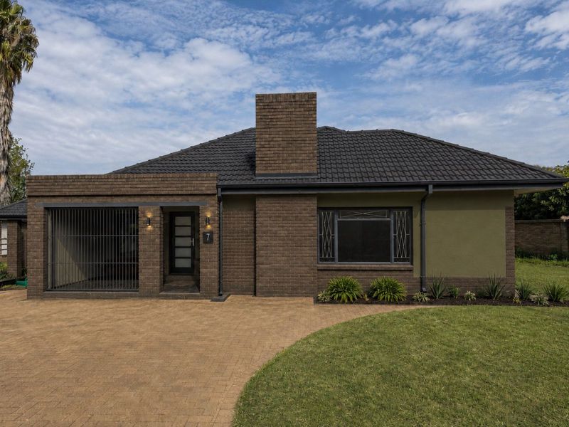A well-maintained single-story brick house featuring a paved driveway, secure entrance, and a prominent chimney, set within a neat garden.